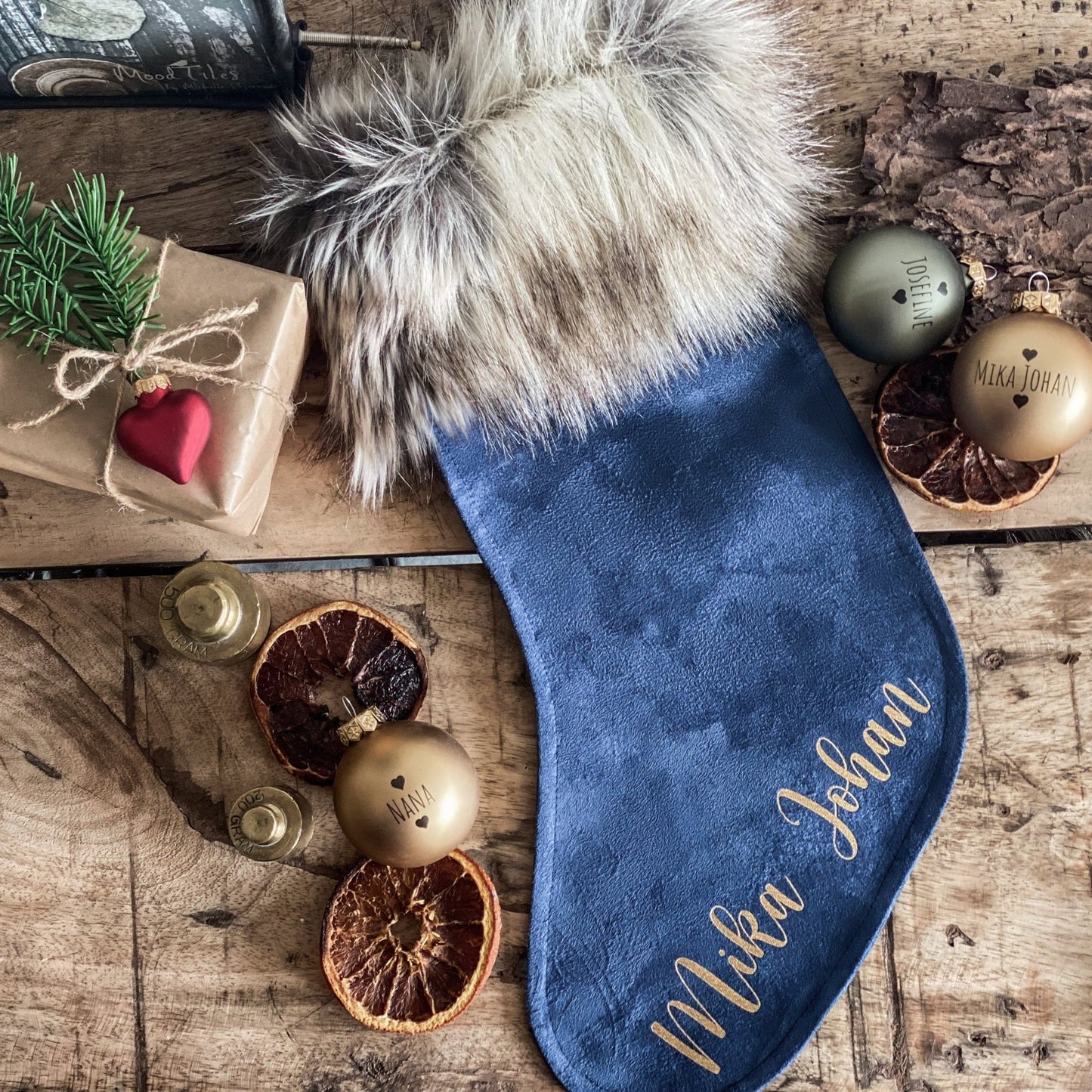 Blå julesok med navn, som ligger på et gammelt bord bed pakker og julekugler