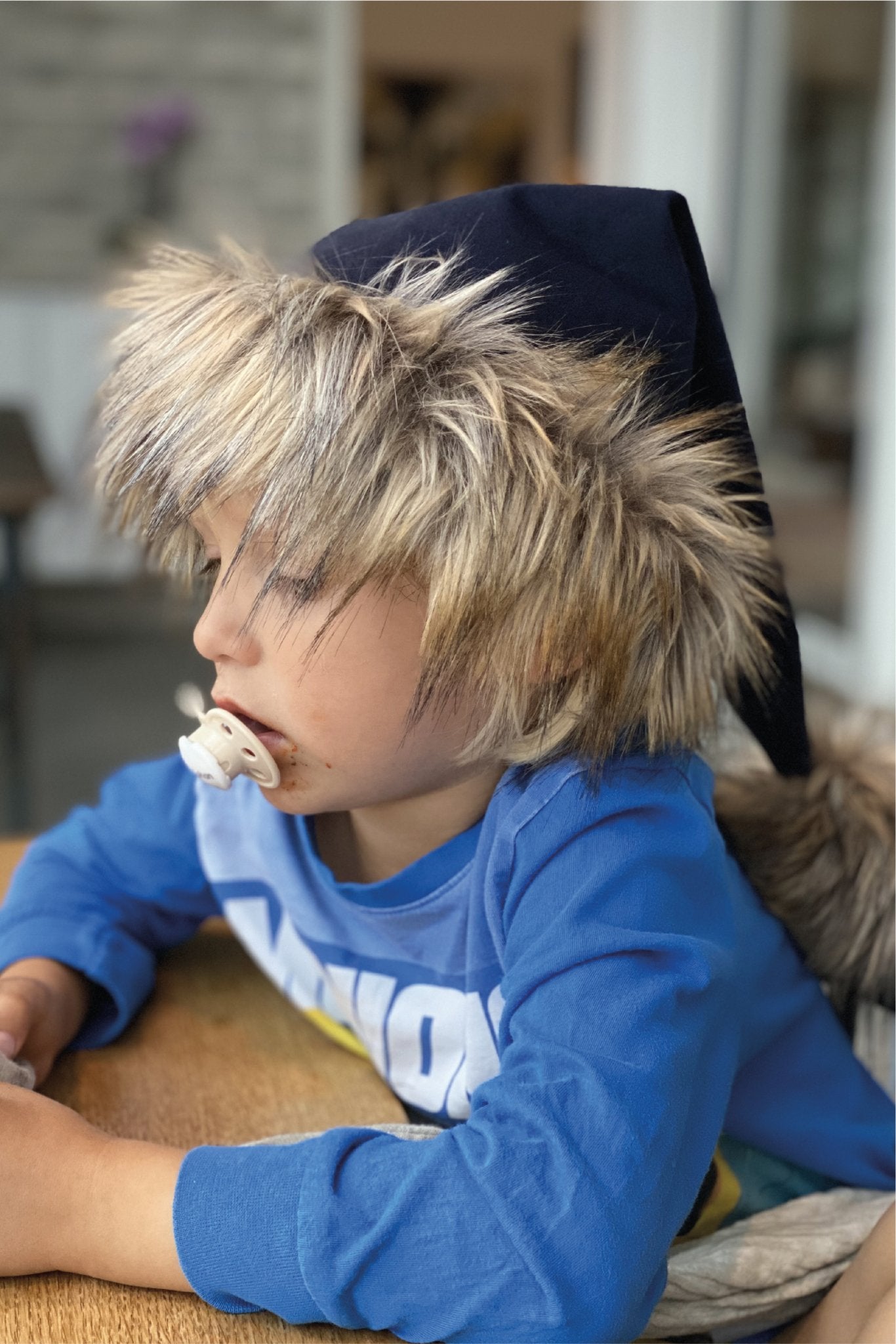 Sød nissehue i blå til børn, Her ses nissehuen på en lille 3 årig dreng. Nissehuen er lavet af mørkeblå velour og har en pelskant og stor kvast lavet i imiteret ulvepels