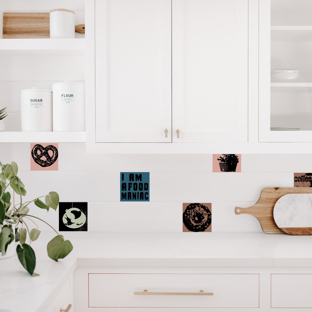 Flisestickers og kaldet fliseklistermærker fra MoodTIles. Her ses Flisestickers med billeder af kaffe og kage sat op i et hvidt køkken, på nogle få af vægfliserne.